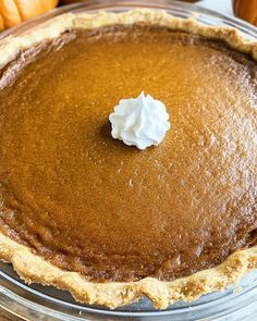 a pumpkin pie with whipped cream on top in a glass pie dish, surrounded by other pumpkins