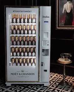 a vending machine with lots of champagne bottles in front of a painting on the wall