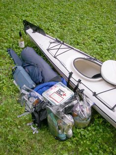 a white kayak is laying on the grass with its lid open and water bottles in it