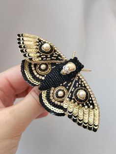 a hand holding a black and gold butterfly brooch with pearls on it's wings