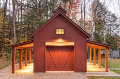 a small red barn with two doors and windows on the front, surrounded by trees