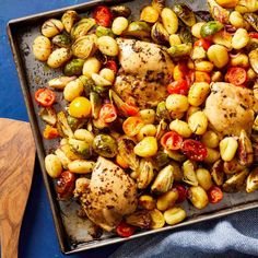 a pan filled with chicken and vegetables on top of a blue table cloth next to a wooden spatula