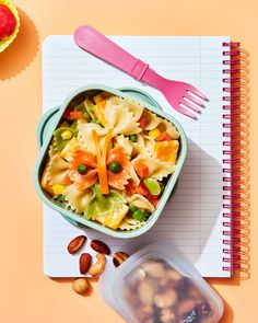 a bowl of pasta with peas and almonds next to a notebook on a table