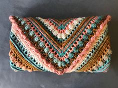 a multicolored crocheted pillow sitting on top of a gray floor next to a wall