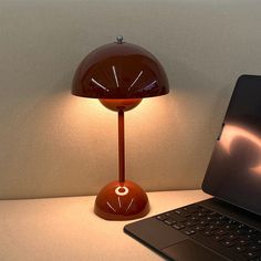 a laptop computer sitting on top of a desk next to an orange table lamp with a red shade