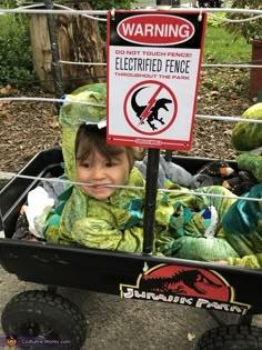 a young child in a wagon with stuffed animals and a sign warning of electric fence