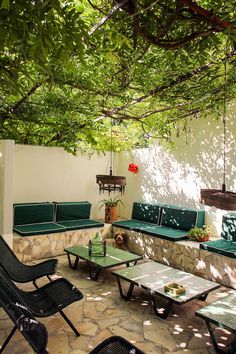 an outdoor seating area with green chairs and tables under a tree covered pergoline