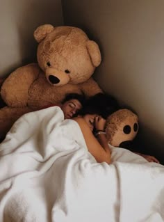 a woman laying in bed next to a large teddy bear with her head on the pillow