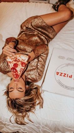 a woman laying on top of a bed holding a slice of pizza