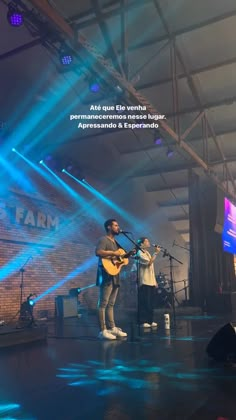 two people playing guitar on stage in front of blue and green lights with words above them