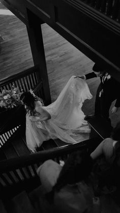 a bride and groom sitting on a bench in black and white with their veil blowing