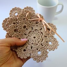 a hand holding some crocheted doily next to a cup