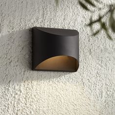 a modern outdoor light mounted on the side of a white stucco wall with a green plant in the corner