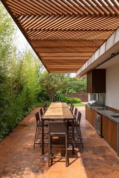 an outdoor kitchen and dining area with wooden table and chairs under a pergolated roof