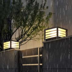 two lights that are sitting on the side of a building in the rain at night