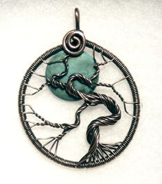 a wire wrapped pendant with a tree on it's side and a green stone in the center