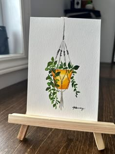 a card with a painting of a plant hanging from it's side on a wooden stand