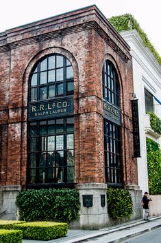 an old brick building with many windows on the outside and people walking by in front