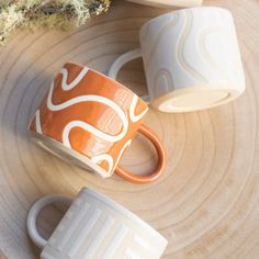 two orange and white coffee cups sitting on top of a wooden table next to a plant