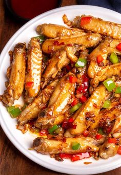 a white plate topped with chicken wings covered in sauce and green peppers next to a cup of tea