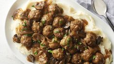 a white plate topped with mashed potatoes and meatballs covered in mushroom gravy