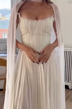 a woman wearing a white dress and veil in front of a window with her hands on her hips