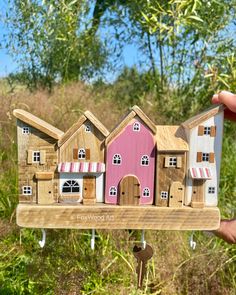 a person holding up a small wooden model of a house with pink roof and windows