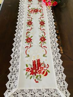 a white table runner with red candles and poinsettis on it, sitting on a wooden table