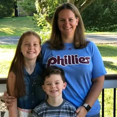 a woman and two children are posing for a photo on a porch with trees in the background