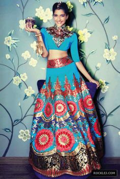 a woman in a blue and red dress standing next to a wall with flowers on it