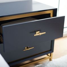 a black and gold dresser with two drawers on it's sides, in front of a window