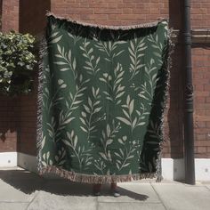 a green and white blanket hanging on a pole next to a brick wall with a plant pattern