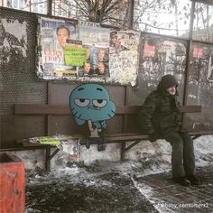 a man sitting on a bench in front of a wall covered with posters and flyers