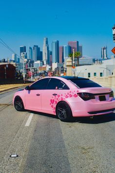 a pink car parked on the side of the road in front of a city skyline