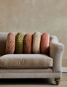 a couch with four different colored pillows sitting on it's back end, in front of a beige wall