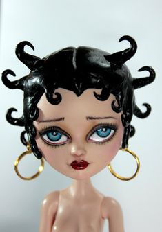 a close up of a doll with blue eyes and black hair wearing large gold hoop earrings