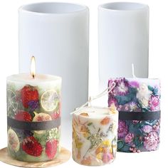 three candles decorated with fruit and flowers are on a white surface next to each other