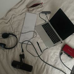 an open laptop computer sitting on top of a bed next to headphones and wires