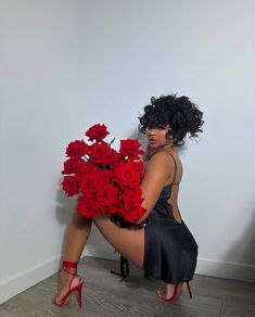 a woman kneeling on the floor with red roses in her lap and holding it up