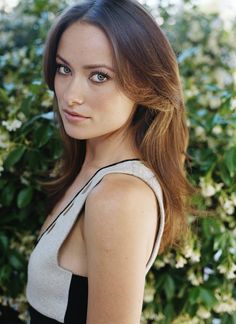 a beautiful young woman standing in front of some bushes