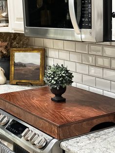 a potted plant sitting on top of a wooden cutting board in front of a microwave