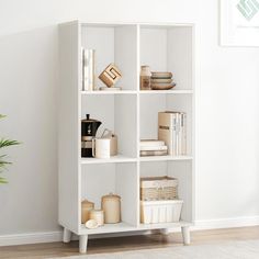 a white book shelf with books and other items on it in a room next to a potted plant