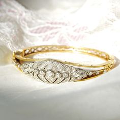 An astounding Edwardian era diamond cluster hinge bangle bracelet in 14k yellow gold and platinum. Features an ornate diamond-encrusted platinum navette setting mounted on a tapered gold band with cutout embellishments and a latch box clasp. Built into the focal point of this bracelet is 5 round-cut diamonds secured in a horizontal line of bezel settings. The open work on either side of the platinum setting is also decorated with three prong-set diamond accents. All the diamonds seem to be in go Classic Diamond Cuff Bracelet For Formal Occasions, Classic Cuff Bracelet With Diamond Accents, Classic Cuff Bracelet With Brilliant Cut For Anniversary, Elegant Diamond Cut Cuff Bracelet For Anniversary, Diamond Cut Diamond Cuff Bracelet For Anniversary, Elegant Rose Cut Diamond Bracelets For Formal Occasions, Anniversary Brilliant Cut Cuff Bracelet, Classic Single Cut Diamond Cuff Bangle Bracelet, Classic Single Cut Diamond Cuff Bangle