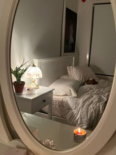 a mirror reflecting a bed with white sheets and pillows in front of a night stand