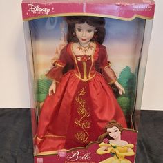 the doll is in its box and has a red dress with gold trimmings