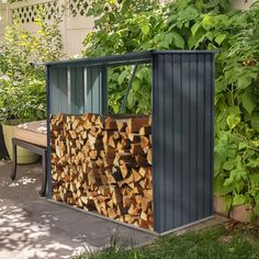 a large pile of firewood sitting next to a garden shed in the middle of a yard