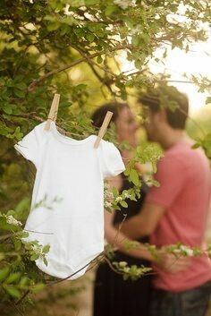 a man and woman standing next to each other in front of trees with clothes hanging from them