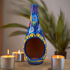 a blue vase sitting on top of a wooden table next to candles and a potted plant