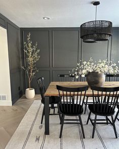 a dining room table with black chairs and white flowers in a vase on the floor