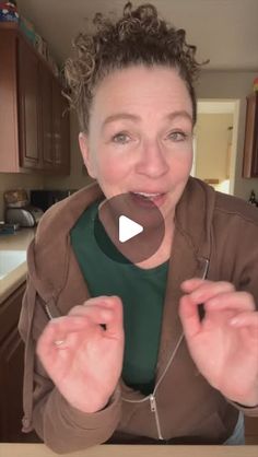 a woman standing in front of a kitchen counter holding her hands up to the camera